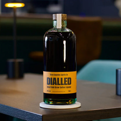 Dialled Decaf Cold Brew Coffee Liqueur bottle on a wooden table with blurred lounge background